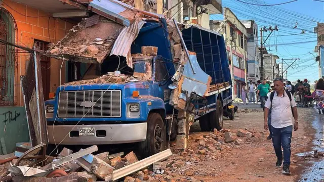 Um homem passa ao lado de um caminhão que está com vários pedaços de telha e tijolos por cima. 