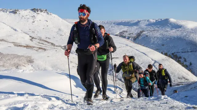 Los corredores de resistencia con bastones de trekking suben una pendiente empinada en la nieve.