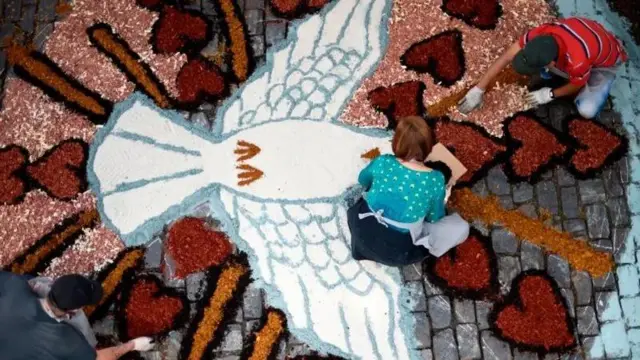 Foto de cima mostra uma mulher no chão fazendo um tapete de Corpus Christi em uma rua.