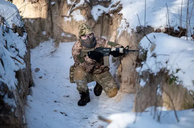 Một phụ nữ mặc quân phục, cầm súng trường tự động, ngồi trong chiến hào trong một cuộc huấn luyện quân sự dành cho dân thường, ngày 12/1/2024 tại Kyiv, Ukraine.
