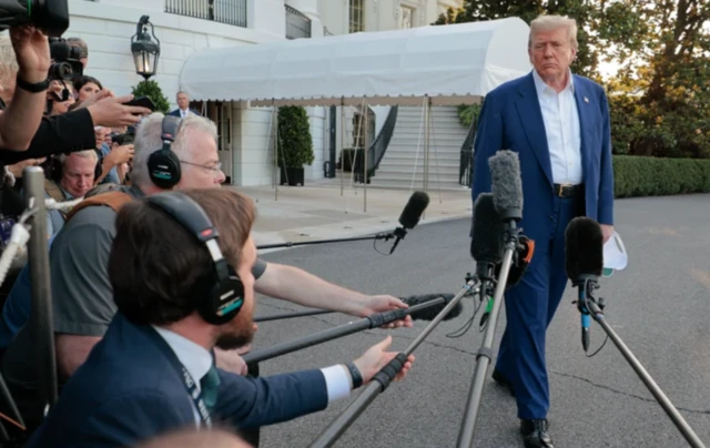 Trump gazetecilerin uzattığı kimi sopanın ucundaki mikrofonlara bakıyor.