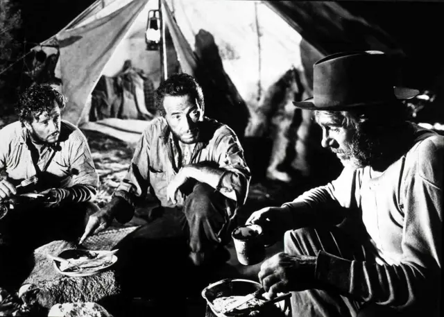 Tim Holt, Humphrey Bogart y Walter Houston frente a una carpa, comiendo a la intemperie, en una escena de "El Tesoro de la Sierra Madre".