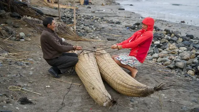 Dois homens manipulando embarcação na praia