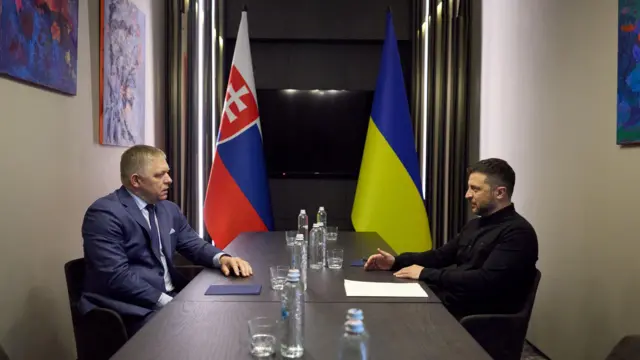 Зеленський та Фіцо сидять за столом один навпроти іншого, за ними - прапори України та Словаччини