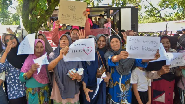 Sejumlah warga membawa poster saat menyambut kedatangan Presiden Prabowo Subianto di Nagari Kayu Tanam, Padang Pariaman, Sumatera Barat, Kamis (18/12/2025).
