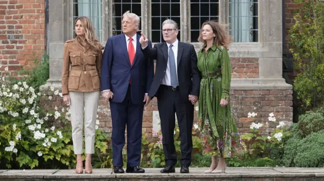 Мелания Трамп, Дональд Трамп, Кир Стармер и Виктория Стармер наблюдают за показательными прыжками парашютистов. Стармер указывает пальцем вперед.