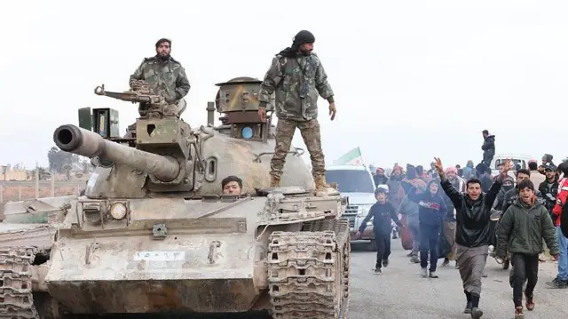 Bir grup Suriye askeri tankın üstünde Halep'in doğusundaki mahallelere giriyor. Tankın yanında ise onları kutlayan siviller görülüyor.