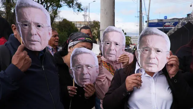 Pessoas na rua com máscaras com rosto de Uribe