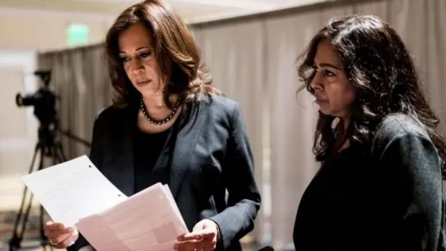 Kamala Harris e Maya Harris, duas mulheres negras de cabelo comprido, de terninho, olham documentos