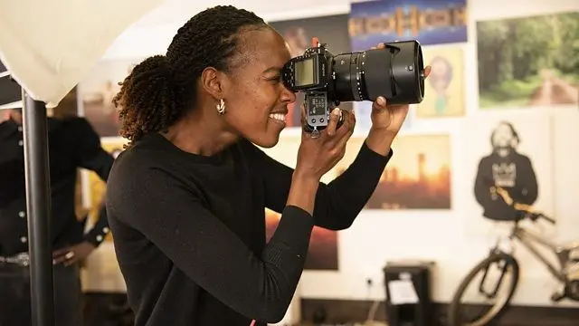 Wata mace sanye da baƙaken tufafi, da kyamarar ɗaukar hoto