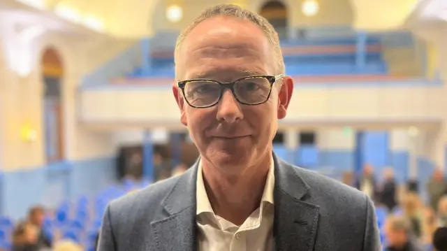 Un hombre con pelo corto y gafas mira a la cámara.