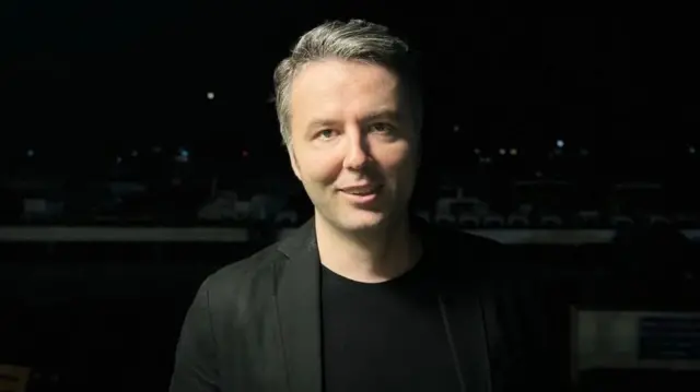 Mehmet Akif Ersoy siyah ceket ve siyah tişörtle poz veriyor.