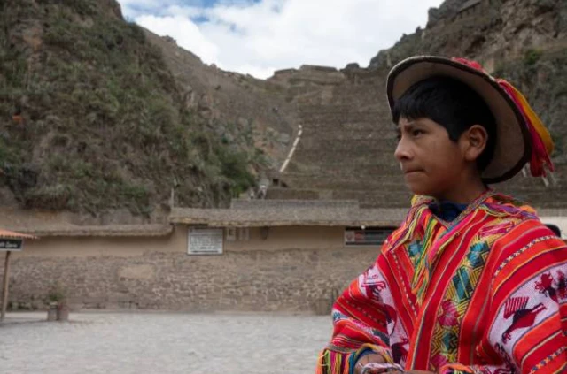เด็กชายชาวเปรูในชุดพื้นเมือง ที่ด้านหน้าโบราณสถานอารยธรรมอินคา Ollantaytambo ในเมืองกุสโก