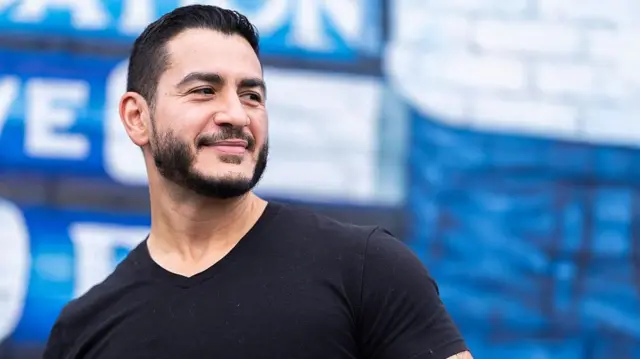 Abdul El-Sayed, vistiendo una camiseta negra, mira con una sonrisa hacia el lado derecho de la pantalla.