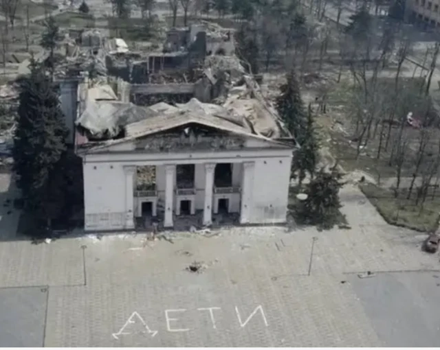 Разбомбленный театр и надпись “Дети” на площади перед ним