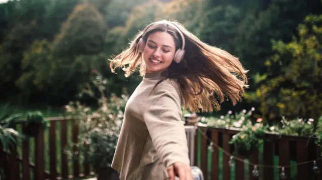 Kobieta słucha muzyki i tańczy w ogrodzie, mając na sobie bezprzewodowe słuchawki.