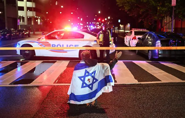 Un hombre con la bandera israelí frente a unos coches de policía.