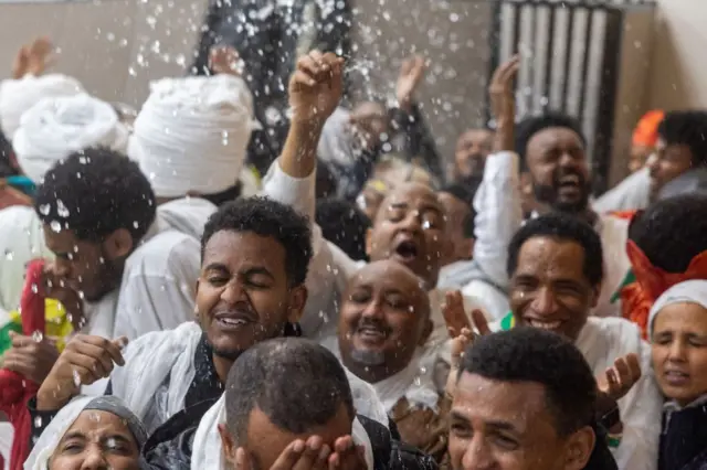 People smile as they are doused with water by clergy at an Ethiopian Orthodox Cathedral.