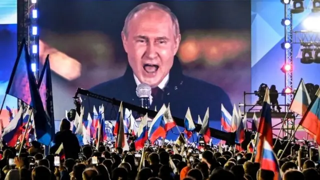 Vladimir Putin speaks to crowds in Moscow, with the words "Together forever" at the top of the screen.
