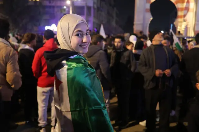 Suriye bayrağını sırtına alan bir kız kameraya gülerek poz veriyor