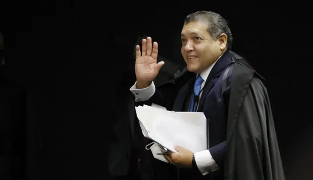 Nunes Marques com toga e papéis na mão, acenando 