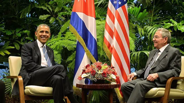 Los presidentes Barack Obama y Raúl Castro sonríen sentados en La Habana junto a las banderas de EE.UU. y Cuba, durante el proceso de normalización de relaciones bilaterales en 2016. 