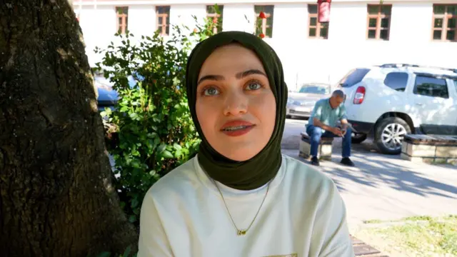 Bahar Kurşun'un üzerinde bej bir tişört, başında yeşil örtü var. 