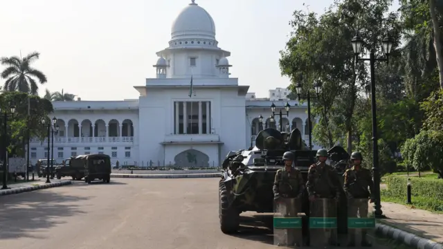 西洋風の白い裁判所の建物正面に広いカープールがあり、迷彩柄の戦車や軍の車両が停まっている。写真手前にある戦車の前には迷彩服とヘルメット姿の兵士が3人、透明な防弾盾を持って並んでいる。カープールの外側の歩道には南国の街路樹や街灯が並んでいる
