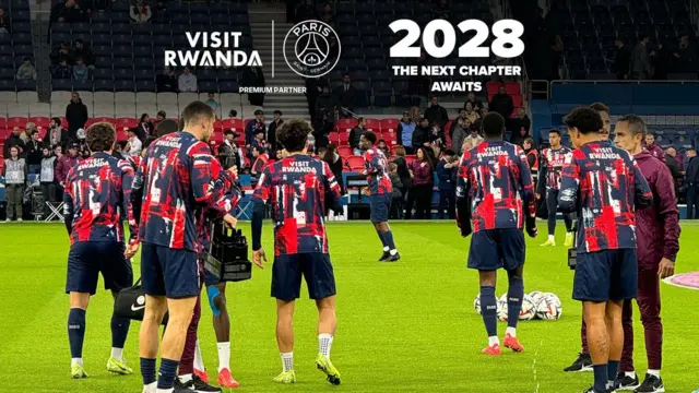 Abakinnyi ba PSG bari mu myitozo mu kibuga bambaye imipira yanditseho 'Visit Rwanda' mu bitugu. Hejuru yabo yari amagambo yuko amasezerano mashya n'u Rwanda azageza mu 2028. Imbere yabo hirya hari abantu ku kibuga bahagaze n'abicaye.