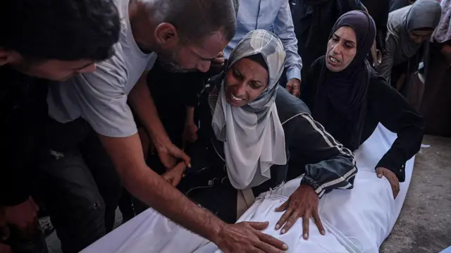 Dos mujeres lloran sobre el cuerpo de un familiar fallecido y amortajado.