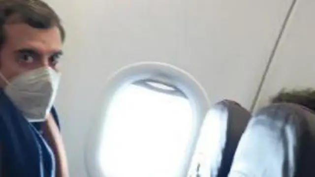 Роман Доброхотов в маске в самолете около иллюминатора.