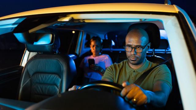 Homem dirigindo carro de aplicativo com passageira à noite
