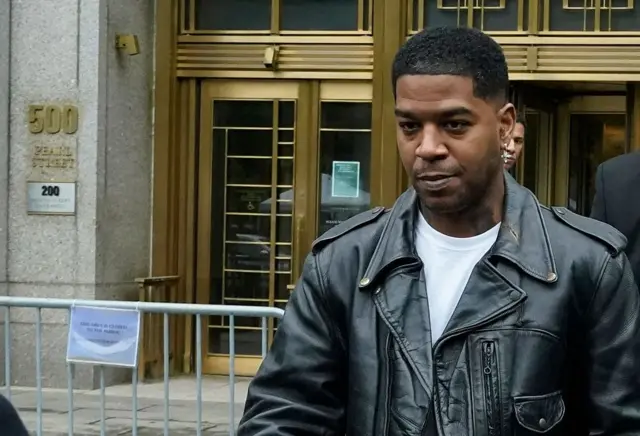 Kid Cudi é um homem negro. Ele está usando uma jaqueta preta