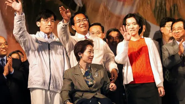 2000年3月18日晚,当选总统陈水扁(后排中间)与家人站在台上,向在台湾总统选举中投票支持民进党的选民致谢。前排就座的是他的妻子吴淑珍,左边是21岁的儿子陈致中,右边是23岁的女儿陈幸妤。最后选举结果公布后,超过100万人聚集在民进党总部外的街道上,庆祝民进党赢得总统大选,结束了台湾长达50年的国民党统治。