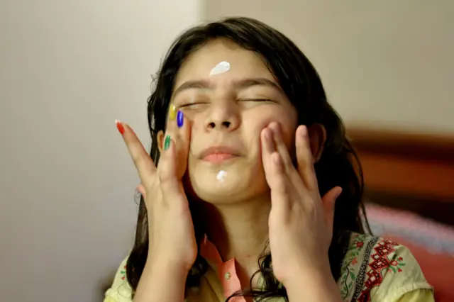 चेहऱ्याला क्रीम लावणारी लहान मुलगी