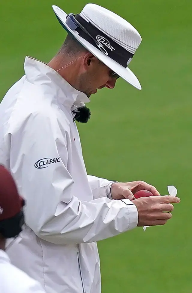 Umpire Micheal Gough uses a wipe to disinfect a bowler's saliva from the ball on the fourth day of the second Test cricket match between England and the West Indies at Old Trafford in Manchester, northwest England on July 19, 2020. (Photo by Jon Super