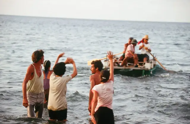 Cubanos deixam a costa em pequenas embarcações enquanto outros, com as pernas dentro da água, acenam em despedida