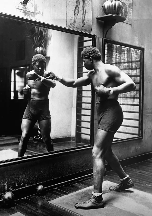 Le boxeur Siki s'entraîne devant un miroir d'un gymnase. 