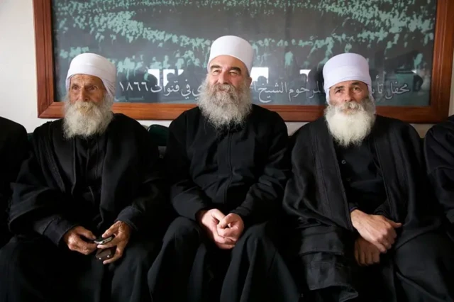 سه شیخ در لباسهای سیاه و کلاه سفید و ریش بلند سفید. شیخ حکمت سلمان هجری در وسط