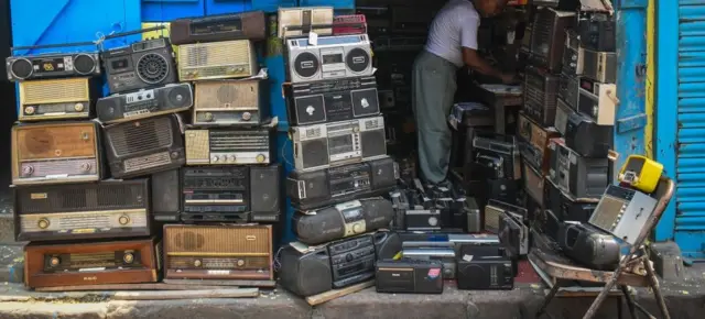 Shagon wani mutum mai gyaran radiyo da tarin radiyoyin a ciki da bakin shagon nasa