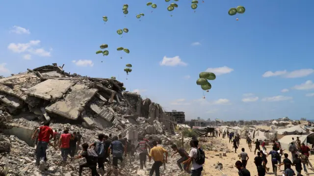 FILE PHOTO: Palestinians run towards parachutes carrying aid packages airdropped over northern Gaza Strip, August 7, 2025. REUTERS/Ebrahim Hajjaj/File Photo