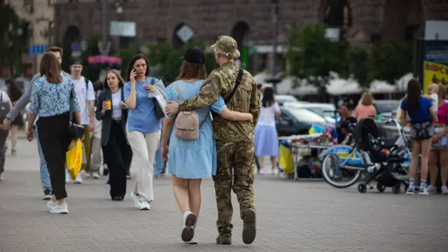 Пара серед натовпу йде по центральній вулиці Києва, хлопець у військовому обіймає дівчину в сукні