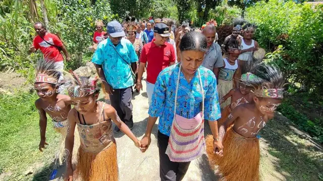 Perempuan papua dengan pakaian adat sedang berjalan.