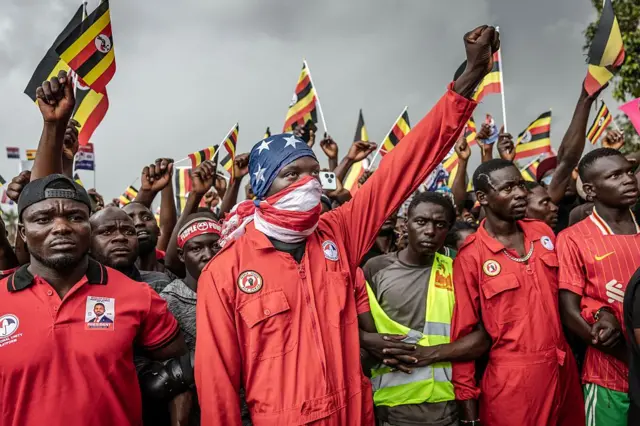 A group of young men wearing red jumpsuits standing in line, fists raised in the air.