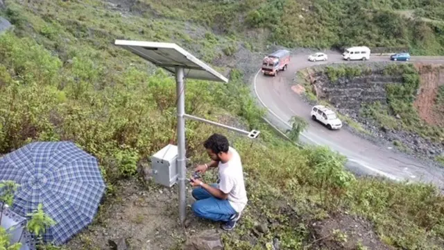 Seorang pria memperbaiki sistem pemantauan longsor di lereng yang menghadap jalan.