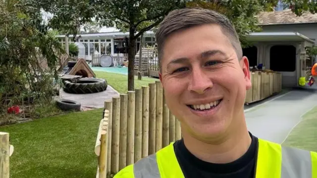 Dallan Tan, de colete, sorrindo em frente a um novo parquinho