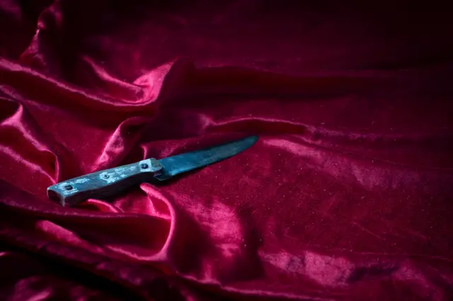 Grande faca sobre roupa de cama rosa e cintilante