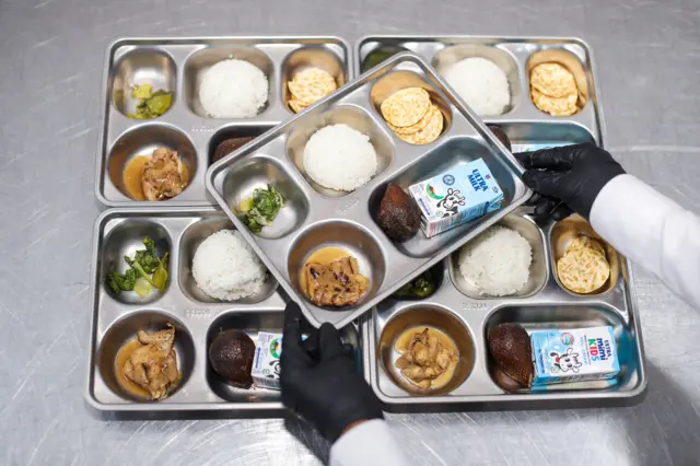 Pekerja menunjukan menu Makanan Bergizi Gratis (MBG) saat proses pemorsian di sebuah Satuan Pelayanan Pemenuhan Gizi (SPPG).