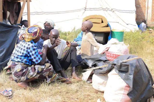 Umuryango w'abakongomani wicaye hagati y'ibintu wahunganye ku kibuga c'umupira w'amaguru ca Rugombo mu ntara ya Cibitoke
