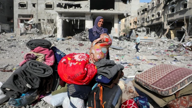 Yıkıntılar arasındaki eşyalarıyla duran bir kadın